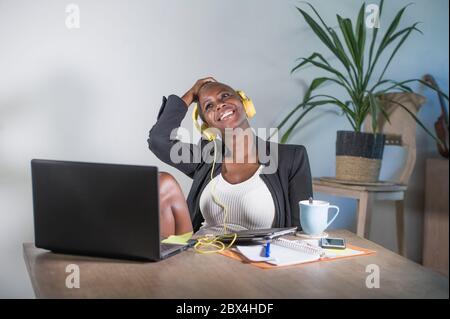 Junge glückliche schwarze Afro amerikanische Frau Musik mit Kopfhörern hören aufgeregt und freudig arbeiten am Laptop-Computer-Schreibtisch an einem modernen Arbeitsplatz im Bus Stockfoto