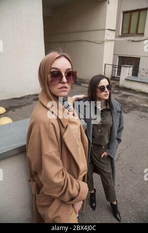 Outdoor-Mode-Aufnahme von zwei schönen stilvollen Damen in trendigen warmen Outfits. Attraktive weibliche Models posieren vor der Kamera im Hintergrund der Stadt Stockfoto