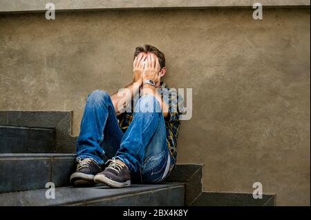Junge traurige und verzweifelte Mann sitzt draußen an der Straße Treppe leiden Angst und Depression Gefühl elend Weinen in Arbeitslosigkeit und aufgegeben Stockfoto