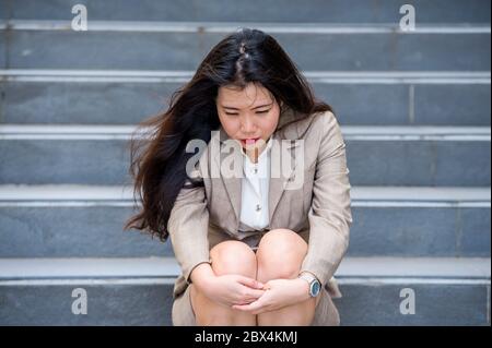 Junge depressive und verzweifelte asiatische chinesische Geschäftsfrau weinend allein auf der Straße Treppe leiden Stress und Depression Krise Opfer Stockfoto