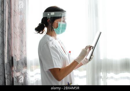 Krankenschwester mit Gesichtsschutz mit einer Tablette. Seitenansicht Stockfoto