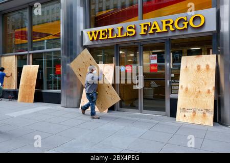 New York, New York, 2. Juni 2020. Arbeiter, die eine Bankfiliale von Wells Fargo in Midtown Manhattan nach einer Serie von großen, organisierten Einbrüchen/Plünderungen in der Stadt betreten haben. Die Bank schließt sich anderen Unternehmen in der ganzen Stadt an, die Angst vor Plündern haben, indem sie vorsorglich Fenster und Türen einsteigen und gleichzeitig eine Botschaft der Hoffnungslosigkeit und Verzweiflung an viele senden, die es nicht gewohnt sind, so viele verschlossene Ladenfronten in einer normalerweise lebhaften und geschäftigen Stadt zu sehen. Die Bank blieb während der COVID-19-Coronavirus-Pandemie offen und hatte weniger Dienste. Juni 2020 Stockfoto