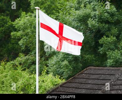 Die englische rote Kreuzfahne von St. George flattert über einem Haus mit einem Wald im Hintergrund. Stockfoto