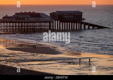 Cromer Pier bei Sonnenuntergang mit Menschen, die am Strand spazieren. Stockfoto