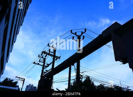 Silhouette Bild von elektrischen Pol mit Stromleitungen und Kabeltrasse vom Transformator an das Gebäude, blauen Himmel und den Mond im Hintergrund verbunden Stockfoto