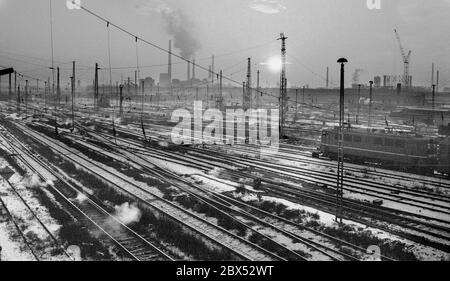 Sachsen-Anhalt / DDR Land / Winter / Dezember 1989 Winterabend in Bitterfeld, Sonnenuntergang hinter dem Braunkohlekombinat, Bahngelände vor // Stimmung / Wirtschaft / Vertrauen / Industrie / Landschaft 1894 die Firma Chemische Fabrik Griesheim (Frankfurt am Main) Baut in Bitterfeld eine Fabrik zur Herstellung von chloriertem Kalk durch Elektrolyse. 1900 wurde das Verfahren auch zur Gewinnung von Magnesium und Aluminium eingesetzt, 1923 zog Griesheim komplett nach Bitterfeld. In der Nähe der Braunkohlebergwerke siedelten sich weitere Firmen an: Agfa baute eine Farb- und eine Folienfabrik. 1990 ging das Ende. Das VEB Chemiekombinat Stockfoto
