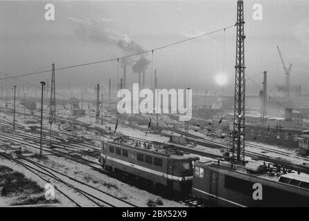 Sachsen-Anhalt / DDR / Winter / Dezember 1989 Winterabend in Bitterfeld, Sonnenuntergang hinter dem Braunkohlekombinat, Bahngelände vor // Stimmungen / Wirtschaft / Vertrauen / Industrie / 1894 die Firma Chemische Fabrik Griesheim (Frankfurt am Main) Baut in Bitterfeld eine Fabrik zur Herstellung von chloriertem Kalk durch Elektrolyse. 1900 wurde das Verfahren auch zur Gewinnung von Magnesium und Aluminium eingesetzt, 1923 zog Griesheim komplett nach Bitterfeld. In der Nähe der Braunkohlebergwerke siedelten sich weitere Firmen an: Agfa baute eine Farb- und eine Folienfabrik. 1990 kam das Ende. Das VEB Chemiekombinat hatte noch 13000 Stockfoto