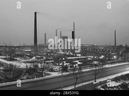 Sachsen-Anhalt / DDR Land / Winter / Dezember 1989 Winterabend in Bitterfeld, Sonnenuntergang hinter dem Braunkohlekombinat, Bahngelände vor // Stimmung / Wirtschaft / Vertrauen / Industrie / Landschaft 1894 die Firma Chemische Fabrik Griesheim (Frankfurt am Main) Baut in Bitterfeld eine Fabrik zur Herstellung von chloriertem Kalk durch Elektrolyse. 1900 wurde das Verfahren auch zur Gewinnung von Magnesium und Aluminium eingesetzt, 1923 zog Griesheim komplett nach Bitterfeld. In der Nähe der Braunkohlebergwerke siedelten sich weitere Firmen an: Agfa baute eine Farb- und eine Folienfabrik. 1990 ging das Ende. Das VEB Chemiekombinat Stockfoto