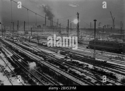 Sachsen-Anhalt / DDR Land / Winter / Dezember 1989 Winterabend in Bitterfeld, Sonnenuntergang hinter dem Braunkohlekombinat, Bahngelände vor // Stimmung / Wirtschaft / Vertrauen / Industrie / Landschaft 1894 die Firma Chemische Fabrik Griesheim (Frankfurt am Main) Baut in Bitterfeld eine Fabrik zur Herstellung von chloriertem Kalk durch Elektrolyse. 1900 wurde das Verfahren auch zur Gewinnung von Magnesium und Aluminium eingesetzt, 1923 zog Griesheim komplett nach Bitterfeld. In der Nähe der Braunkohlebergwerke siedelten sich weitere Firmen an: Agfa baute eine Farb- und eine Folienfabrik. 1990 ging das Ende. Das VEB Chemiekombinat Stockfoto
