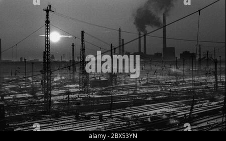 Sachsen-Anhalt / DDR Land / Winter / Dezember 1989 Winterabend in Bitterfeld, Sonnenuntergang hinter dem Braunkohlekombinat, Bahngelände vor // Stimmung / Wirtschaft / Vertrauen / Industrie / Landschaft 1894 die Firma Chemische Fabrik Griesheim (Frankfurt am Main) Baut in Bitterfeld eine Fabrik zur Herstellung von chloriertem Kalk durch Elektrolyse. 1900 wurde das Verfahren auch zur Gewinnung von Magnesium und Aluminium eingesetzt, 1923 zog Griesheim komplett nach Bitterfeld. In der Nähe der Braunkohlebergwerke siedelten sich weitere Firmen an: Agfa baute eine Farb- und eine Folienfabrik. 1990 ging das Ende. Das VEB Chemiekombinat Stockfoto