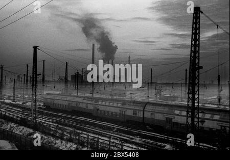 Sachsen-Anhalt / DDR Land / Winter / Dezember 1989 Winterabend in Bitterfeld, Sonnenuntergang hinter dem Braunkohlekombinat, Bahngelände vor // Stimmung / Wirtschaft / Vertrauen / Industrie / Landschaft 1894 die Firma Chemische Fabrik Griesheim (Frankfurt am Main) Baut in Bitterfeld eine Fabrik zur Herstellung von chloriertem Kalk durch Elektrolyse. 1900 wurde das Verfahren auch zur Gewinnung von Magnesium und Aluminium eingesetzt, 1923 zog Griesheim komplett nach Bitterfeld. In der Nähe der Braunkohlebergwerke siedelten sich weitere Firmen an: Agfa baute eine Farb- und eine Folienfabrik. 1990 ging das Ende. Das VEB Chemiekombinat Stockfoto