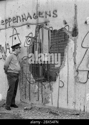 Berlin-Bezirk / DDR / Wall / 1990 Kreuzberg: DDR-Volkspolizisten schauen durch das Loch in der Mauer nach Westen, gehackt von Mauerspechten, die Tag und Nacht Stücke aus der antiimperialistischen Mauer der DDR hacken. Es gibt nichts mehr zu bewachen. Hinter der Mauer ist Kreuzberg // Grenze / Vereinigung / DDR / Bezirke / Geschichte / Kommunismus [automatisierte Übersetzung] Stockfoto