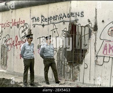 Berlin-Bezirk / DDR / Wall / 1990 Kreuzberg: DDR-Volkspolizisten schauen durch das Loch in der Mauer nach Westen, gehackt von Mauerspechten, die Tag und Nacht Stücke aus der antiimperialistischen Mauer der DDR hacken. Es gibt nichts mehr zu bewachen. Hinter der Mauer ist Kreuzberg // Grenze / Vereinigung / DDR / Bezirke / Geschichte / Kommunismus [automatisierte Übersetzung] Stockfoto