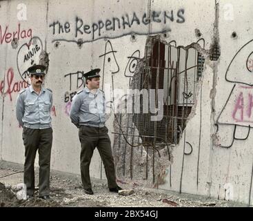 Berlin-Bezirk / DDR / Wall / 1990 Kreuzberg: DDR-Volkspolizisten schauen durch das Loch in der Mauer nach Westen, gehackt von Mauerspechten, die Tag und Nacht Stücke aus der antiimperialistischen Mauer der DDR hacken. Es gibt nichts mehr zu bewachen. Hinter der Mauer ist Kreuzberg // Grenze / Vereinigung / DDR / Bezirke / Geschichte / Kommunismus [automatisierte Übersetzung] Stockfoto