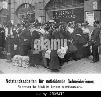 Die bedürftigen Näherinnen liefern ihre öffentlichen Hilfswerke im Berliner Bekleidungsviertel ab. Als Millionen von Männern bei Kriegsausbruch eingezogen wurden, fehlen viele der Hauptverdiener der Familien. Die staatlichen Mittel haben dies nicht ausreichend kompensiert. Deshalb hat der Staat Hilfswerke und Dienstpflichten geschaffen, um zu helfen. Im Hintergrund, der Laden H.Czapski. An der Wand ist ein Plakat mit einer Ankündigung über die öffentliche Arbeit in der Bekleidungsindustrie. Stockfoto