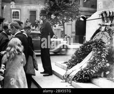 Ein Polizist steht Wache neben dem Londoner Cenotaph, während Passanten sich Blumenkränze ansehen, die deutsche Veteranen dort zum Gedenken an die Opfer des Ersten Weltkriegs gelegt haben. Eine Parade der deutschen Veteranen zum zuvor abgesagten Denkmal fand statt, statt im Royal Hospital in Chelsea. Stockfoto