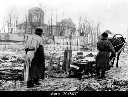 Zwei deutsche Soldaten ziehen einen Schlitten mit abfallenem Proviant durch die umkreiste Stadt Cholm. Im Hintergrund ist die bombardierte Kirche der Stadt. Während der Einkreisungsschlacht von Kholm verteidigte die Kampfgruppe Scherer die Stadt erfolgreich für 105 Tage. (Ein Foto der Propaganda Company (PK) des Kriegsberichterstatters Richard Muck, der Anfang März in die Tasche flog). Stockfoto