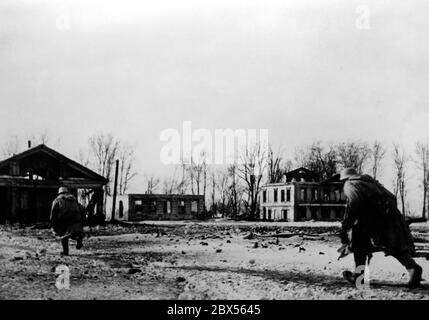 Zwei deutsche Infanteristen überqueren einen Platz, um in einem zerstörten Haus Deckung zu nehmen. Während der Einkreisungsschlacht von Kholm verteidigte die Kampfgruppe Scherer die Stadt erfolgreich für 105 Tage. (Ein Foto der Propaganda Company (PK) des Kriegsberichterstatters Richard Muck, der Anfang März in die Tasche flog). Stockfoto