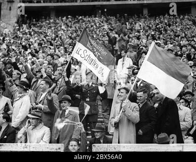 Fans des FC Schalke 04 jubeln beim Finale der Deutschen Fußball-Meisterschaft gegen Admira Wien im Berliner Olympiastadion um ihre Mannschaft. Ein Luftwaffensoldat schwingt die Flagge mit der Aufschrift Schalke 04 - Großdeutscher Meister. In der Mitte sind zwei Luftwaffensoldaten. Stockfoto