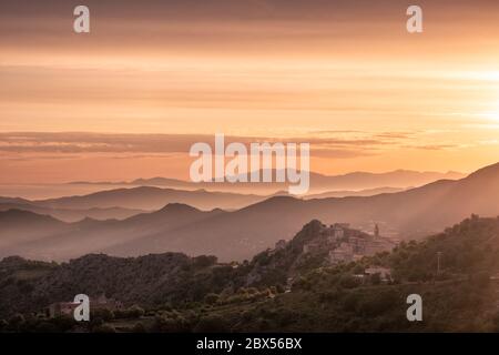 Die Sonne geht über der Silhouette der Küste von Cap Corse und dem alten Bergdorf Speloncato auf Korsika auf Stockfoto