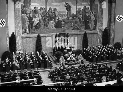 Blick auf die Feierlichkeiten anlässlich des "Tages der nationalen Erhebung" in der Neuen Aula der Friedrich-Wilhelms-Universität Berlin während einer Rede von Gestüt.phil. Assmann. Hinter dem Rednerpult steht ein Porträt Adolf Hitlers. Daneben ist eine Hakenkreuzfahne und die Flagge der NSDStB. Stockfoto