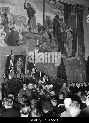 Der Rektor der Universität Berlin, Professor Willy Hoppe (am Pult in Kleid), begrüßt die Anwesenden bei einer Feier zum 5. Jahrestag des "Tags der nationalen Erhebung" in der Neuen Aula. Hinter ihm steht ein Porträt Adolf Hitlers. Stockfoto