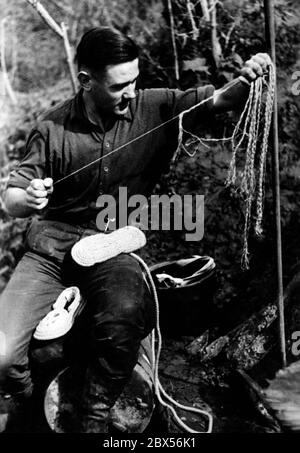 Ein deutscher Soldat macht Schuhe aus den Schnüren eines Fallschirms. Während der Schlacht von Kholm verteidigte die Kampfgruppe Scherer die Stadt 105 Tage lang erfolgreich. (Ein Foto der Propaganda Company (PK) des Kriegsberichterstatters Richard Muck, der Anfang März in die Tasche flog). Stockfoto