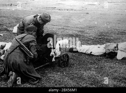 Der Flugplatz in Cholm wurde erst im Mai schneefrei. Zwei Wehrmachtssoldaten inspizieren eine Waffe (vermutlich ein 10.5 cm Leichtschütz 40), daneben liegt ein gefallener sowjetischer Soldat. Während der Umkreisschlacht von Cholm verteidigte die Kampfgruppe Scherer die Stadt erfolgreich für 105 Tage. (Ein Foto der Propaganda Company (PK) des Kriegsberichterstatters Richard Muck, der Anfang März in die Tasche flog). Stockfoto