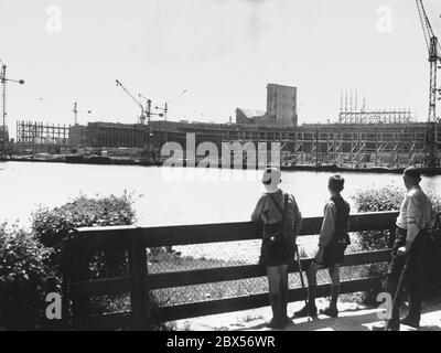 Ein Mann (mit Krücke) und zwei Jungen blicken über den Großen Dutzendteich auf die Baustelle der von den Architekten Ludwig Ruff und Franz Ruff auf dem Reichsparteiengelände in Nürnberg geplanten Kongresshalle. Stockfoto