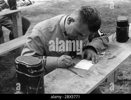 Im Zeltlager der Gau Sachsen der politischen Führer der NSDAP schreibt ein Parteifunktionär zwei Postkarten vom Reichsparteitag in Nürnberg. Neben ihm sind zwei Kochbehälter / Kochgeschirr. Stockfoto