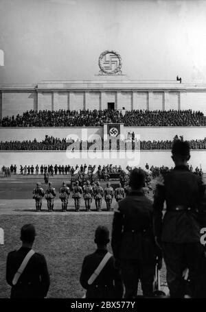 Adolf Hitler, der in seinem Mercedes steht, nimmt den Gruß der Formationen des Reichs-Arbeitsdienstes auf dem Zeppelinfeld während der Nürnberger Kundgebung. Im Hintergrund die Zeppelin Tribüne. Am linken Bildrand und auf der Tribüne befinden sich Filmkameras. Stockfoto