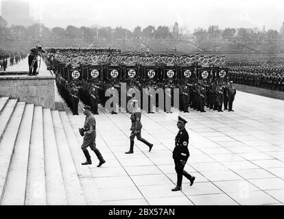 Beim großen Aufruf der SA, SS, NSFK und NSKK in Luitpoldhain gehen Adolf Hitler, Viktor Lutze und Heinrich Himmler von vorne auf die Plattform, vorbei an den Standards der SA und einem Kameramann. Stockfoto