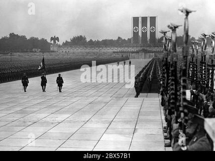 Beim großen Aufruf der SA, SS, NSKK und NSFK in der Luitpold Arena auf dem Reichsparteitagsgelände, nach der Kranzniederlegung am Denkmal, von links nach rechts: Viktor Lutze, Adolf Hitler und Heinrich Himmler kehren zum Podium zurück. Im Vordergrund steht die Blutflagge. Stockfoto