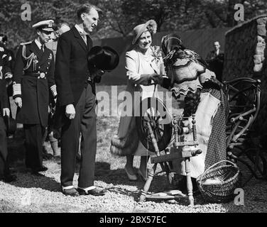 Königin Elizabeth schüttelt während der Empire Exhibition im Bella Houston Park in Glasgow die Hand von Maidie Morrison, einer Frau mit einem Spinnrad aus Barra. König Georg VI. ( hinterließ ) begleitet sie. Stockfoto