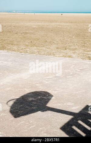 Der Schatten eines Basketball Backboards auf dem Betonboden eines Outdoor-Basketballplatzes am Strand, mit dem Meer im Hintergrund Stockfoto