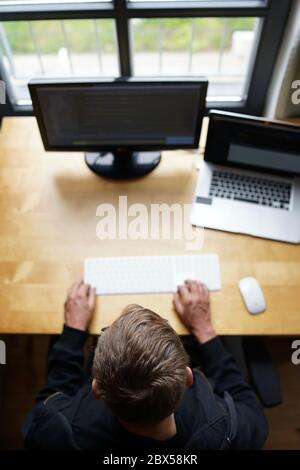 Top-Shot von echten männlichen Web-Programmierer codieren javascript, php, symfony, reagieren, arbeiten mit Tastatur und Maus mit Laptop und externen Monitor von hom Stockfoto