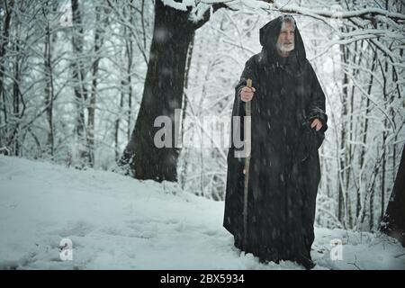 Alte Pilger mit schwarzer Robe in einem verschneiten Wald Stockfoto