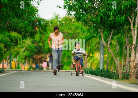 Lifestyle-Porträt der asiatischen indonesischen Mutter und jungen glücklichen Sohn im Stadtpark Spaß zusammen das Kind lernen Fahrrad fahren und die Frau laufen Stockfoto