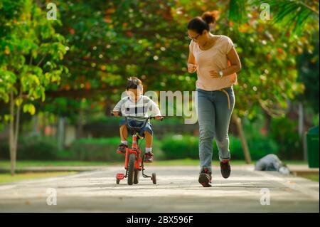 Lifestyle-Porträt der asiatischen indonesischen Mutter und jungen glücklichen Sohn im Stadtpark Spaß zusammen das Kind lernen Fahrrad fahren und die Frau laufen Stockfoto