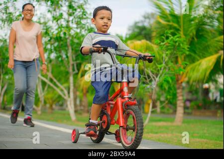 Flifure Porträt der asiatischen indonesischen Mutter und junge glückliche Sohn im Stadtpark Spaß zusammen das Kind lernen Fahrrad fahren und die Frau zu Fuß Stockfoto