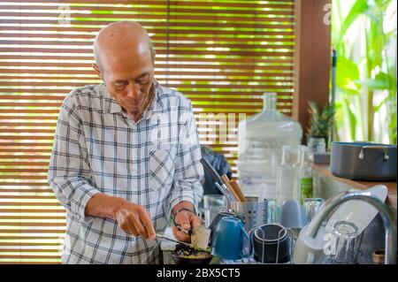 Lifestyle-Porträt von Senior glücklich und süß asiatischen japanischen pensionierten Mann Kochen zu Hause Küche allein ordentlich und ordentlich genießen die Zubereitung von Mahlzeiten in älteren Menschen Stockfoto