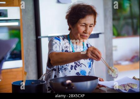 Lifestyle-Porträt von Senior glücklich und süß asiatisch Japanisch Rentner, Frau Kochen zu Hause Küche allein ordentlich und ordentlich genießen Zubereitung von Essen in elde Stockfoto