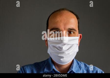 Porträt eines jungen kaukasischen Mannes, der eine schützende Gesichtsmaske vor einem grauen Hintergrund trägt. Studio-Aufnahme mit natürlichem Licht. Stockfoto
