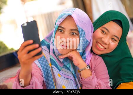 Muslimische Teenager Schüler Freundinnen Selfie. Glücklich und hübsch asiatisch indonesische Mädchen in traditionellen islamischen Hijab Kopf Schal unter Selfie zusammen hav Stockfoto