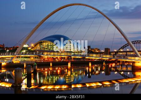 Die Gateshead Millennium Bridge, Sage Center und Newcastles Tyne Bridge, die in der Abenddämmerung in der blauen Stunde mit Lichtern im ruhigen Flusswasser aufgenommen wurde Stockfoto