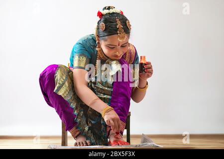 Junge Bharatnatyam Tänzerin sitzt und Anwendung alta auf ihre Füße. Stockfoto