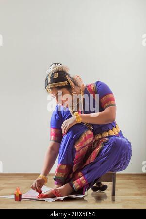 Bharatnatyam Tänzerin sitzt und Anwendung alta auf ihre Füße. Stockfoto