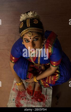 Bharatnatyam Tänzerin sitzt und Anwendung alta auf ihre Füße. Stockfoto