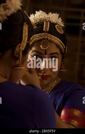 Bharatnatyam Tänzerin schaut sich selbst im Spiegel an und wendet Kajal in ihre Augen an. Stockfoto