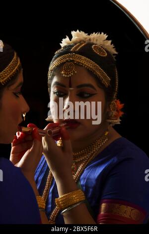 Bharatnatyam Tänzerin schaut sich selbst im Spiegel an und legt Lippenstift auf ihre Lippen. Stockfoto